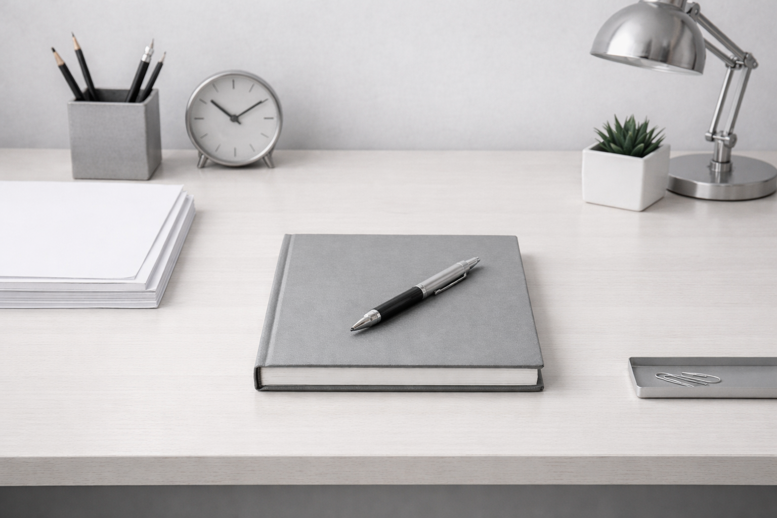 Escritorio de trabajo minimalista con cuaderno, lápiz y objetos alineados sobre una superficie clara.